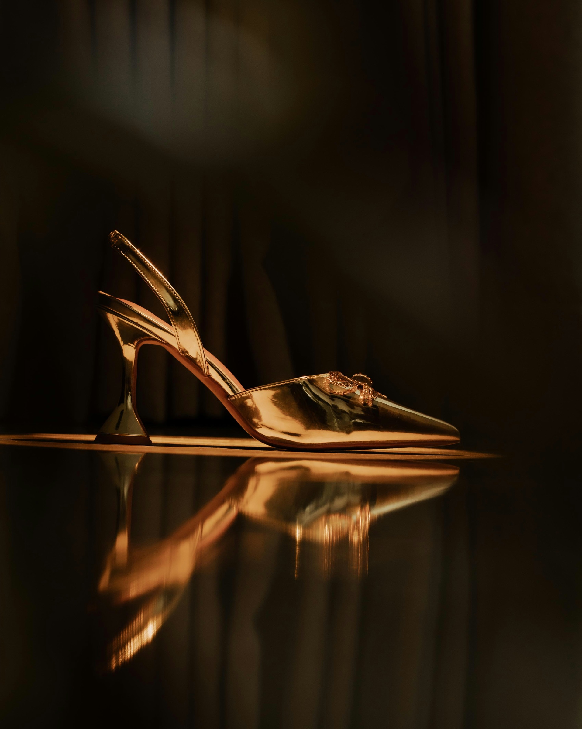 A golden high-heeled shoe reflected on a dark surface